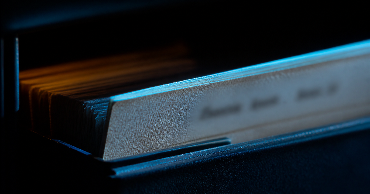 Extreme macro of an index card drawer with one card pulled forward, label illegible, cyan light on the card edges and amber glow deep in the shadow